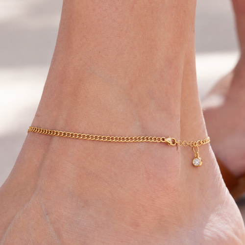 Cora Gold Anklet featuring an 18k gold plated adjustable curb chain adorned with a sparkling crystal charm. 1